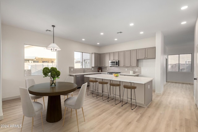 kitchen with gray cabinetry, a center island, hanging light fixtures, light hardwood / wood-style flooring, and stainless steel appliances