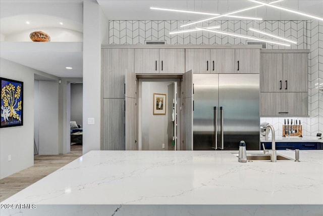 kitchen with light stone counters, light hardwood / wood-style floors, backsplash, stainless steel built in refrigerator, and sink