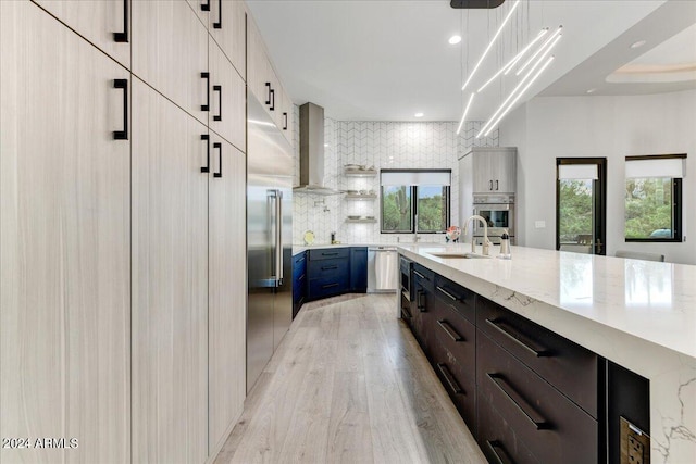 kitchen featuring light wood-type flooring, light stone counters, backsplash, sink, and appliances with stainless steel finishes