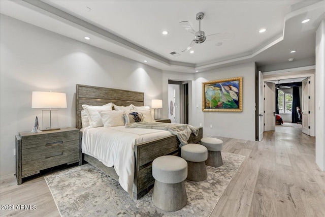 bedroom featuring ceiling fan, light hardwood / wood-style flooring, and a tray ceiling