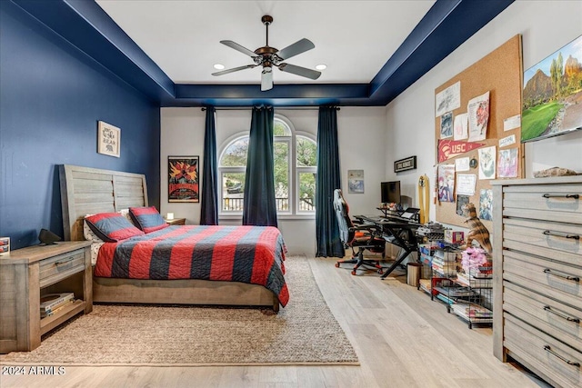 bedroom with light hardwood / wood-style floors, ceiling fan, and a raised ceiling