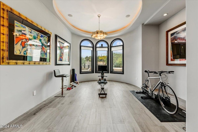 workout room featuring a chandelier, light hardwood / wood-style flooring, and a raised ceiling