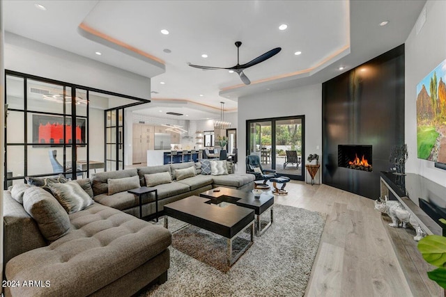 living room featuring light wood-type flooring, ceiling fan, and a raised ceiling