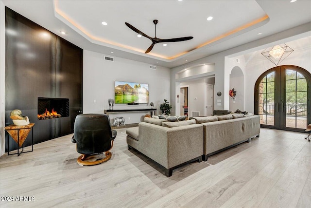 living room with french doors, ceiling fan, light hardwood / wood-style flooring, and a raised ceiling