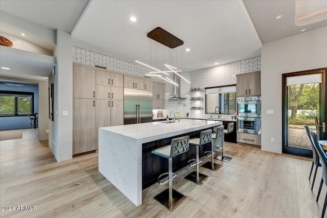 kitchen with light hardwood / wood-style flooring, tasteful backsplash, stainless steel appliances, a center island with sink, and hanging light fixtures