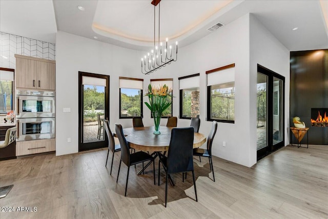 dining room featuring a notable chandelier, a raised ceiling, light hardwood / wood-style floors, and a towering ceiling