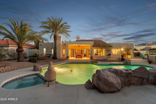 pool at dusk with ceiling fan, an in ground hot tub, fence, a fenced in pool, and a patio area