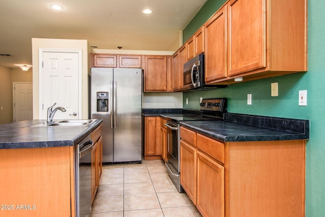 kitchen featuring light tile patterned floors, an island with sink, a sink, appliances with stainless steel finishes, and dark countertops