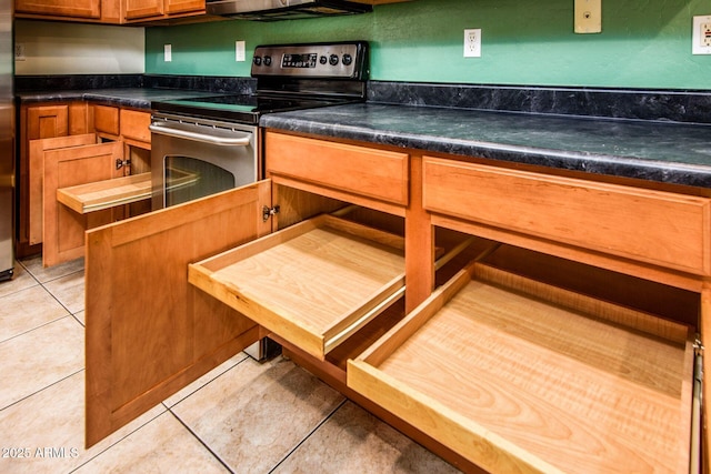 kitchen with light tile patterned floors, electric range, dark countertops, and brown cabinetry