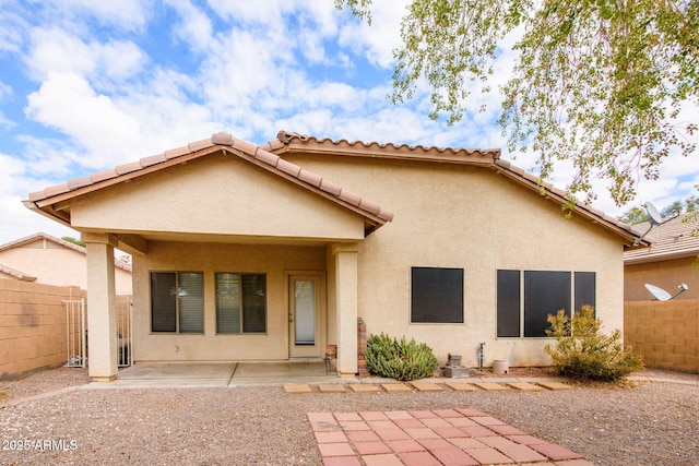 rear view of house with stucco siding, a patio area, and fence