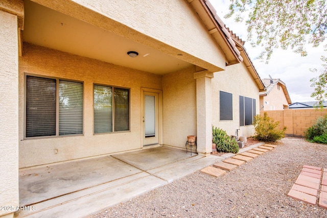 entrance to property featuring stucco siding, a patio, and fence