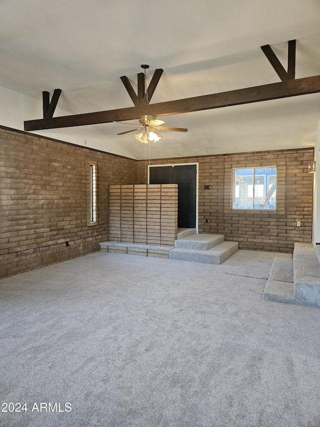 unfurnished living room with carpet flooring, ceiling fan, beamed ceiling, and brick wall