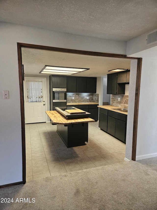 kitchen with light carpet, oven, sink, decorative backsplash, and a kitchen island