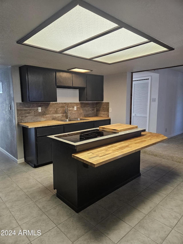 kitchen with wood counters, tasteful backsplash, light tile patterned flooring, and sink