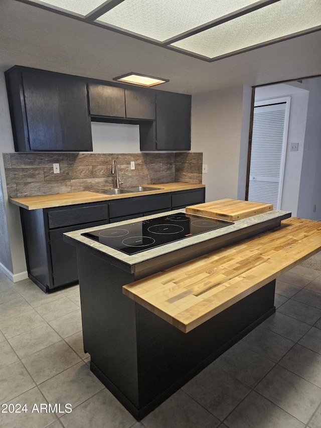 kitchen with light tile patterned flooring, backsplash, butcher block counters, and sink