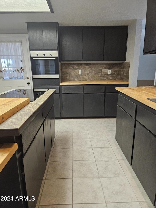 kitchen featuring black electric cooktop, oven, light tile patterned flooring, and butcher block counters