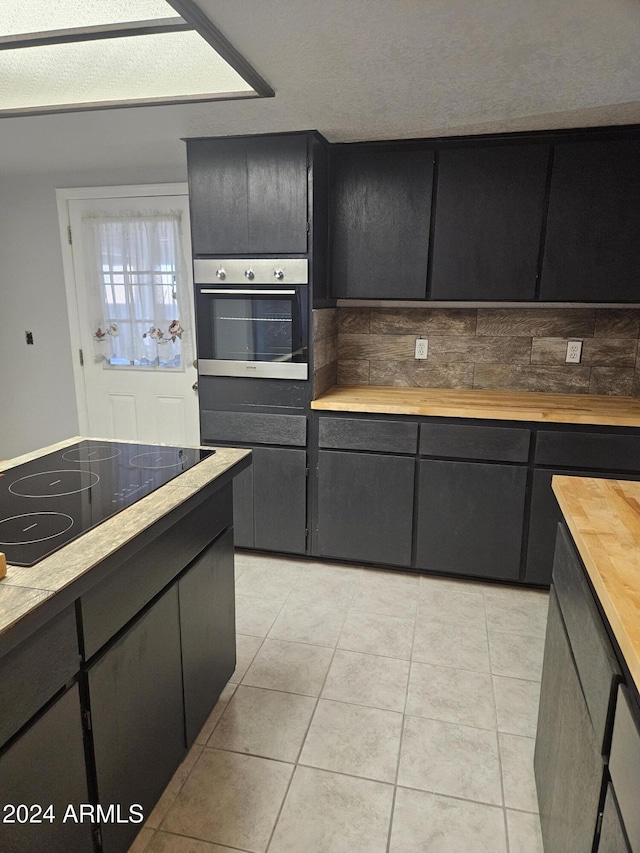 kitchen featuring wooden counters, light tile patterned floors, black electric cooktop, and stainless steel oven