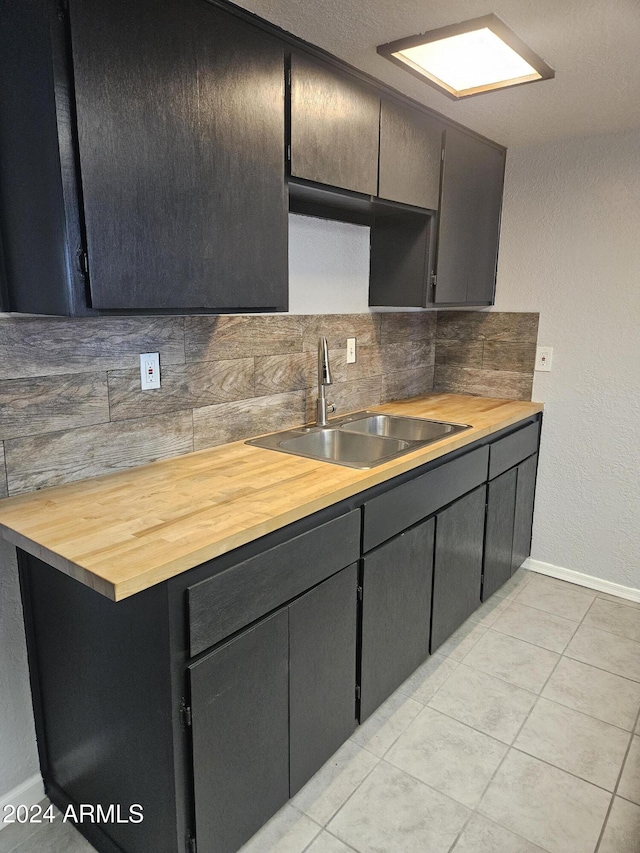 kitchen featuring light tile patterned floors, backsplash, butcher block counters, and sink