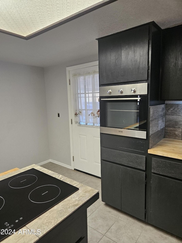 kitchen with stainless steel oven, light tile patterned floors, and black electric stovetop