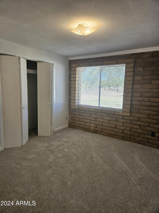 unfurnished bedroom featuring carpet flooring, a textured ceiling, a closet, and brick wall