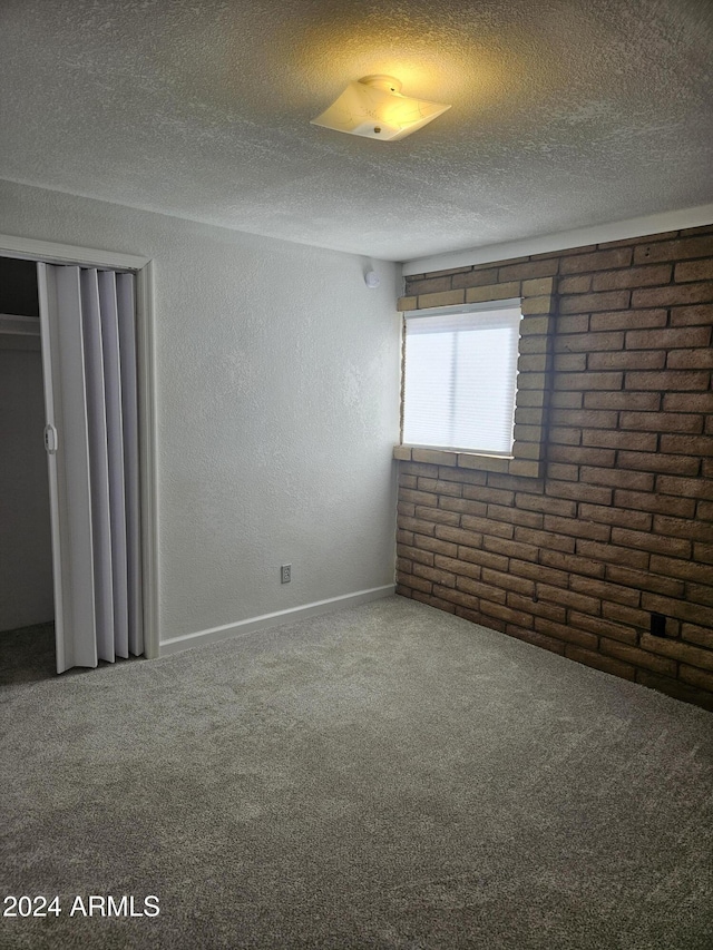 carpeted spare room with brick wall and a textured ceiling