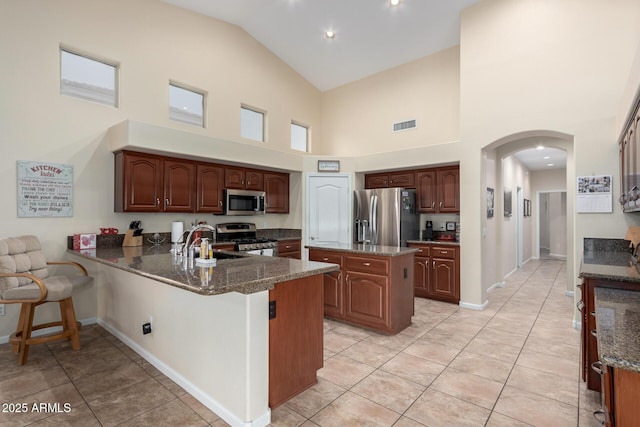 kitchen featuring sink, dark stone countertops, light tile patterned floors, kitchen peninsula, and stainless steel appliances