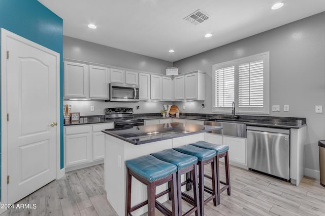 kitchen featuring stainless steel appliances, white cabinetry, sink, a kitchen breakfast bar, and a kitchen island