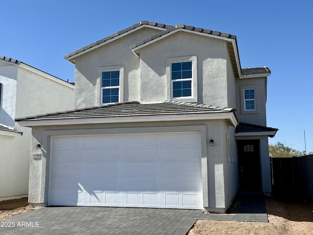 view of front facade featuring decorative driveway, stucco siding, an attached garage, fence, and a tiled roof