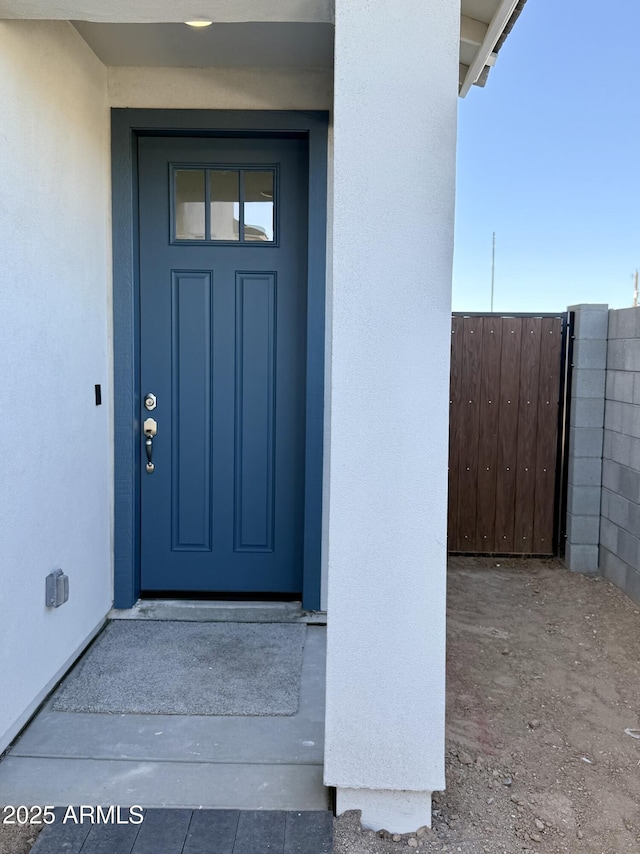 entrance to property featuring fence and stucco siding