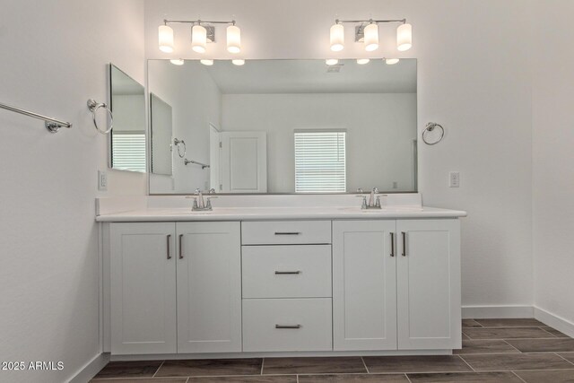 bathroom with double vanity, wood finish floors, a sink, and baseboards