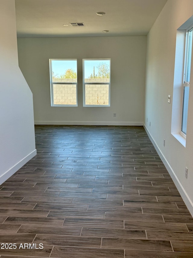 empty room featuring dark wood finished floors, visible vents, and baseboards