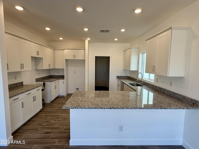 kitchen with dark stone counters, a sink, a peninsula, and wood tiled floor