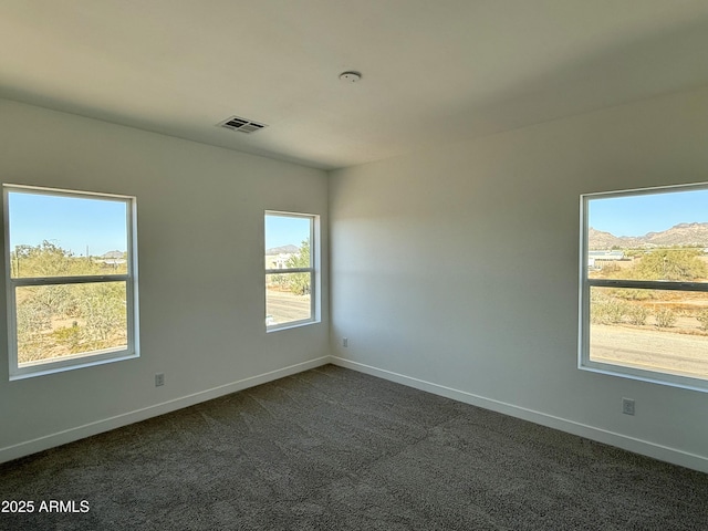 spare room with dark carpet, visible vents, and baseboards