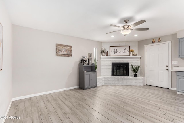 unfurnished living room with light wood-style flooring, recessed lighting, a ceiling fan, baseboards, and a brick fireplace