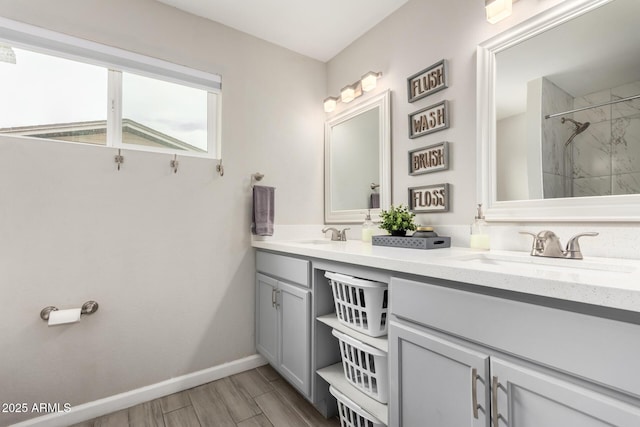 bathroom with wood finish floors, a sink, baseboards, double vanity, and walk in shower