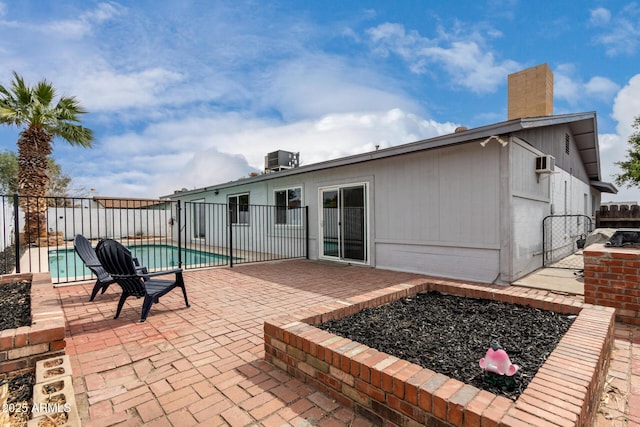 rear view of house featuring a patio, central air condition unit, fence, a fenced in pool, and a chimney