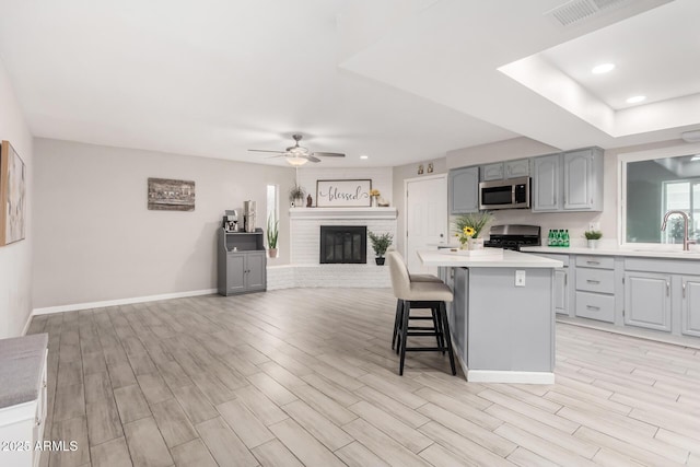 kitchen with gray cabinets, stainless steel microwave, visible vents, range, and a kitchen bar