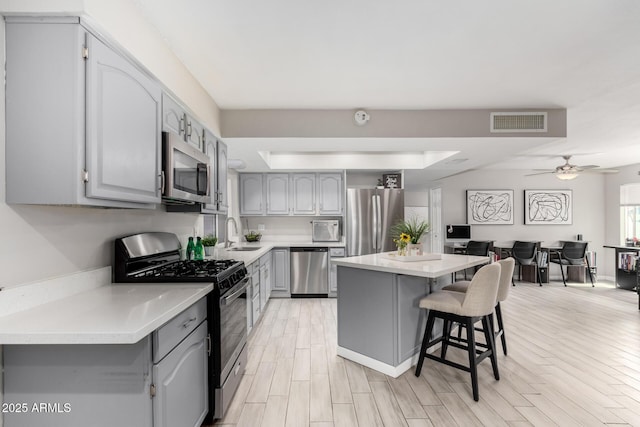 kitchen with visible vents, light wood-style flooring, appliances with stainless steel finishes, a breakfast bar area, and gray cabinets