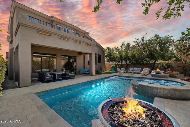 pool at dusk featuring an outdoor living space with a fire pit, a pool with connected hot tub, and a patio area