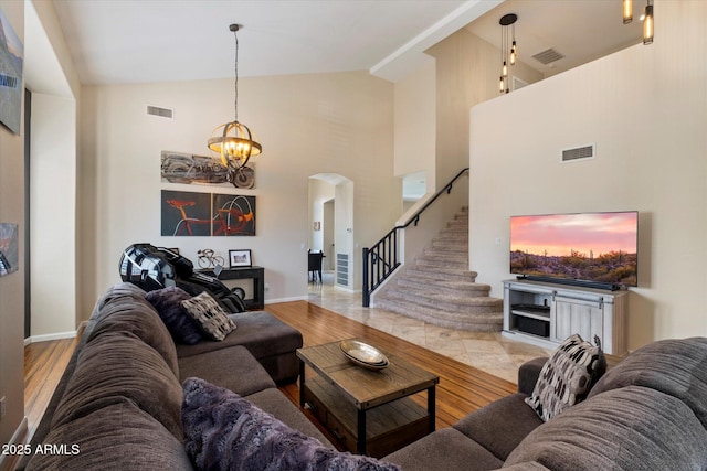 living area featuring arched walkways, high vaulted ceiling, baseboards, stairway, and a chandelier