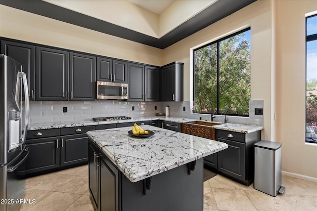 kitchen featuring stainless steel appliances, a sink, backsplash, a kitchen island, and light stone counters