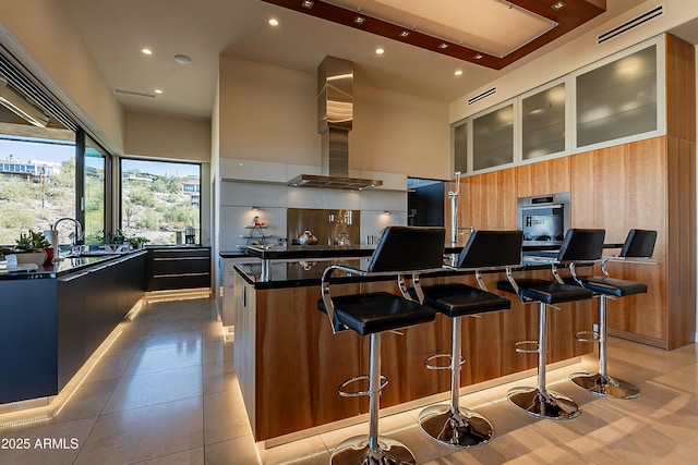 kitchen featuring a towering ceiling, ventilation hood, sink, a kitchen island with sink, and stainless steel oven