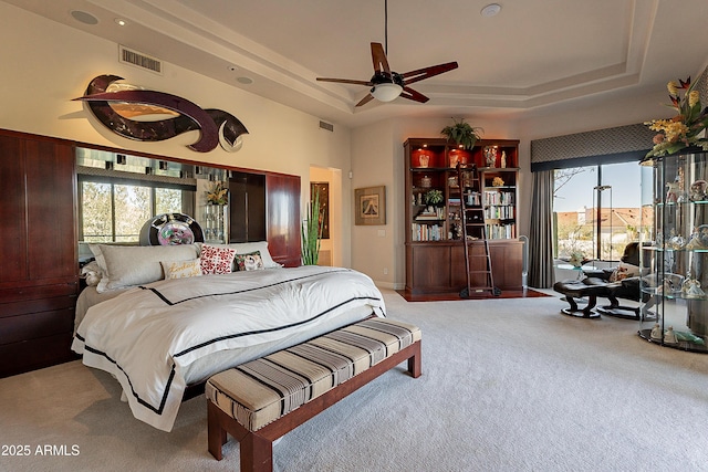 bedroom with a tray ceiling, light colored carpet, and ceiling fan