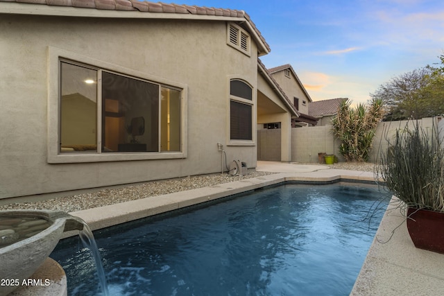 pool at dusk with pool water feature and a patio