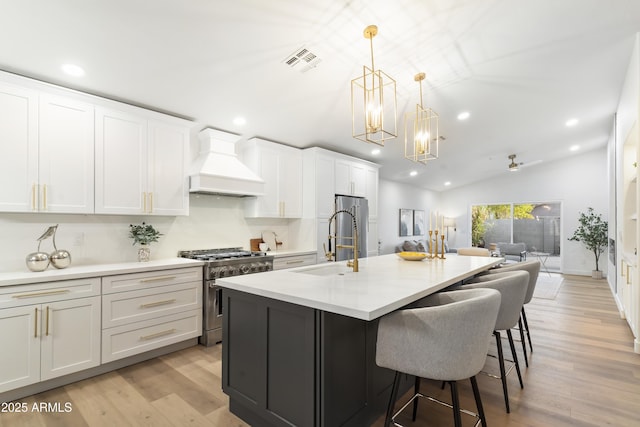 kitchen featuring premium range hood, a kitchen island with sink, hanging light fixtures, premium appliances, and white cabinets