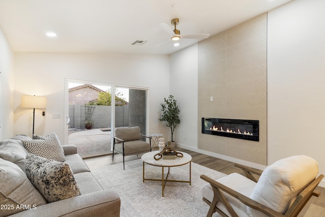 living room with light hardwood / wood-style flooring, a tile fireplace, and ceiling fan