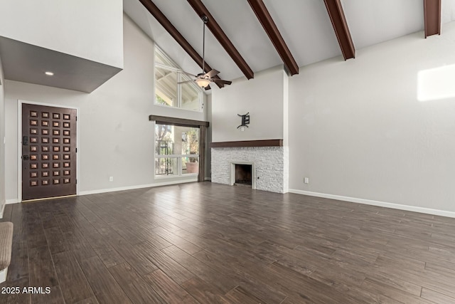 unfurnished living room with dark hardwood / wood-style flooring, ceiling fan, high vaulted ceiling, beamed ceiling, and a stone fireplace