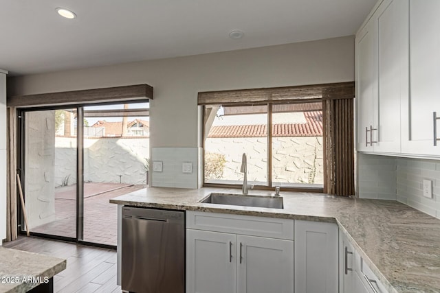 kitchen with sink, stainless steel dishwasher, decorative backsplash, white cabinets, and light wood-type flooring