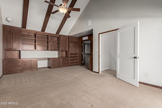 unfurnished living room with ceiling fan, high vaulted ceiling, built in desk, and light colored carpet