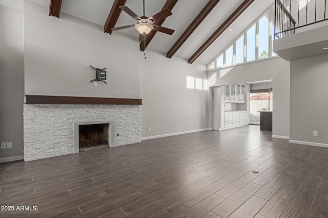 unfurnished living room with beam ceiling, a stone fireplace, ceiling fan, and a towering ceiling